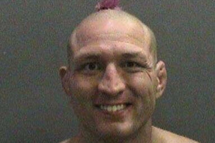 Miller, looking like a war boy from Mad Max, smiles for his mugshot. 