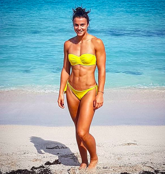 woman at beach in yellow swim suit shows off her muscular body